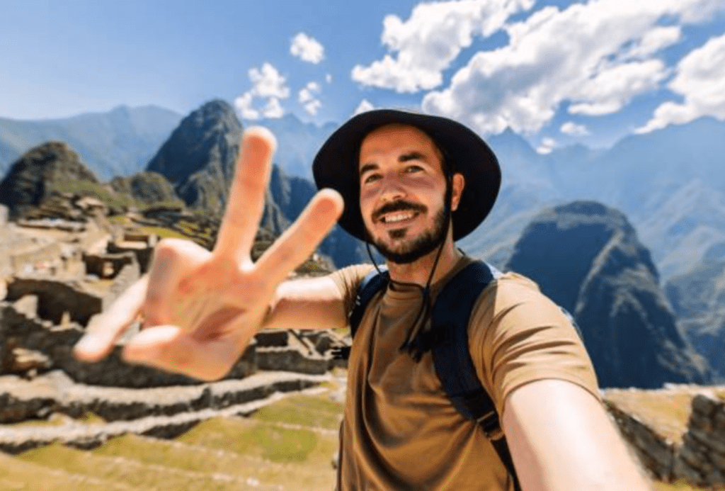 when is the best time to book trips for summer 2025? man doing a peace sign in front of mountains